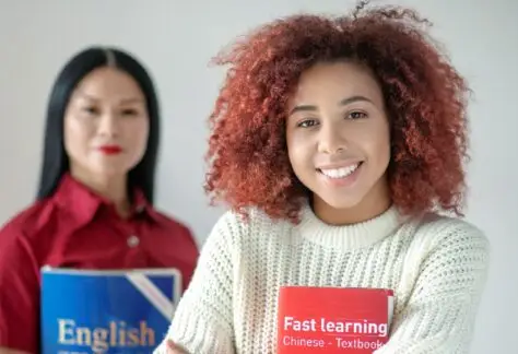 Two females hold books eager to learn